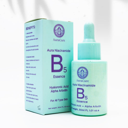 A product image featuring a bottle of Aura Niacinamide B5 Essence next to its packaging box, which is placed on a white surface with a shadow falling across the scene.